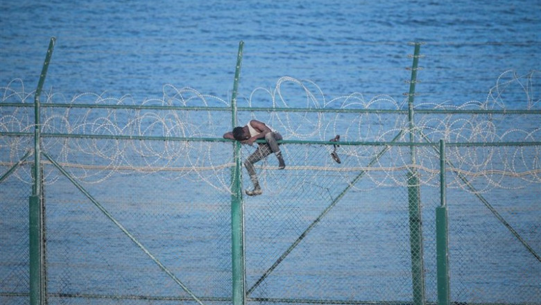 En la imagen, uno de los 153 migrantes, que han entrado en Ceuta saltando su doble valla en la primera incursión en grupo en un año; se aferra a las concertinas. | Antonio Sempere / Europa Press ep en la imagen uno de los 153 migrantes que han entrado en ceuta saltando su doble valla en la