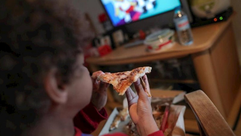 Un niño beneficiario de beca comedor en la Comunidad de Madrid come un trozo de pizza mientras ve la televisión en su casa. | Jesús Hellín - Europa Press ep un nino beneficiario de beca comedor en la comunidad de madrid come un trozo de pizza mientras ve