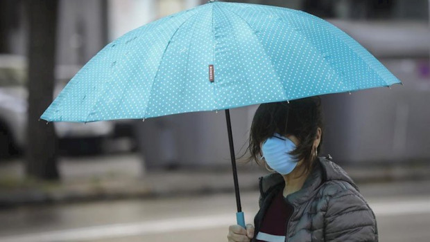 ep una mujer protegida con mascarilla y guantes se resguarda de la lluvia bajo su paraguas en la