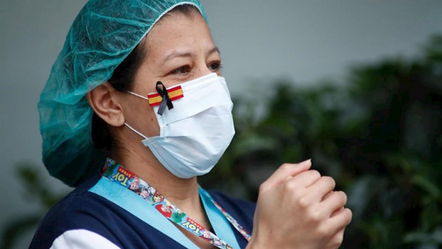 ep una sanitaria con una mascarilla que muestra una bandera de espana con un lazo negro de luto por