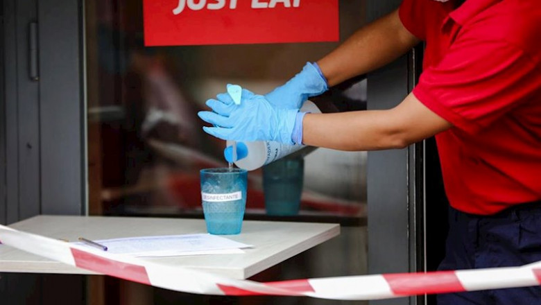 Una trabajadora de Telepizza protegida con una mascarilla y unos guantes de látex, vierte gel desinfectante en un vaso mientras entrega menús infantiles de Telepizza en el barrio de Abrantes, cadena que, junto a Rodilla, reparte un menú escolar a más de 1 | Jesús Hellín - Europa Press ep una trabajadora de telepizza protegida con una mascarilla y unos guantes de latex vierte gel